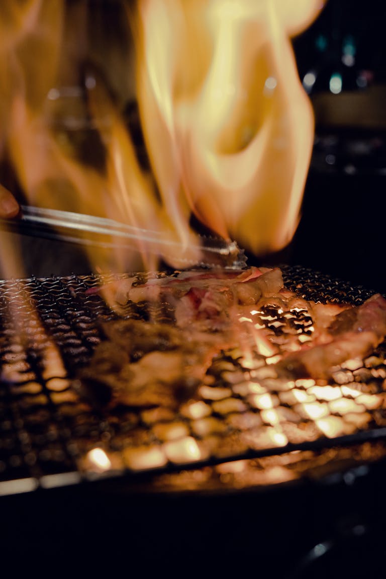 Close-up of meat sizzling on a grill with vibrant flames creating a warm ambiance.